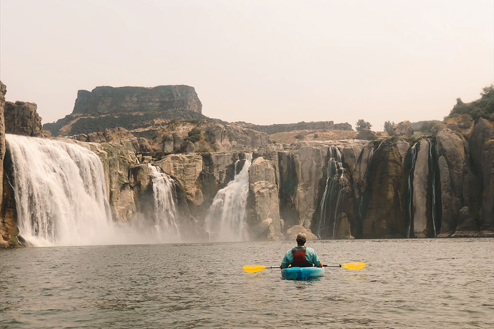 Kayaking on the Snake River in Twin Falls Idaho with waterfalls and canyon cliffs in the background