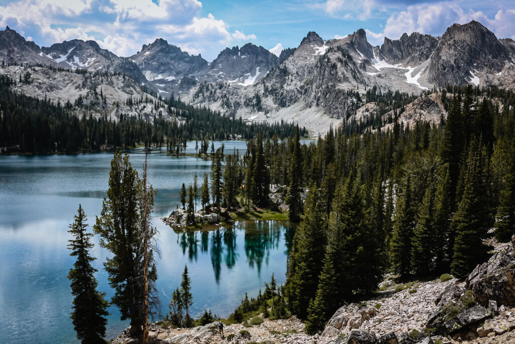 Alice Lake in Idaho surrounded by alpine peaks, evergreen forests, and clear blue water in the Sawtooth Mountains