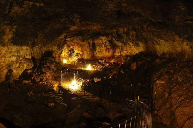 Illuminated walkway inside Idaho’s Mammoth Cave, showing lava-formed rock walls and underground passage way in southern Idaho