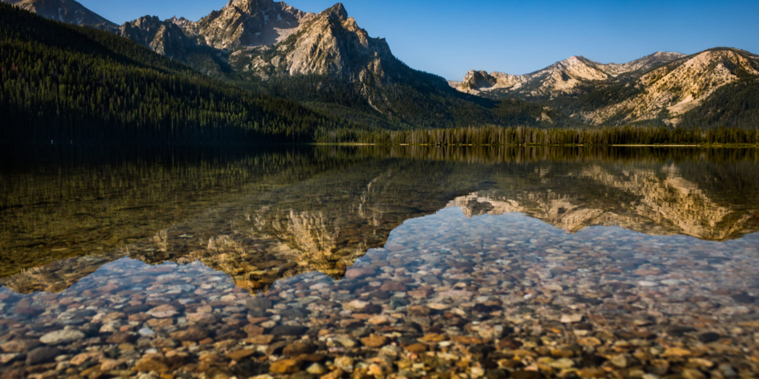 Clear alpine lake in Idaho reflecting rugged mountain peaks and forested slopes