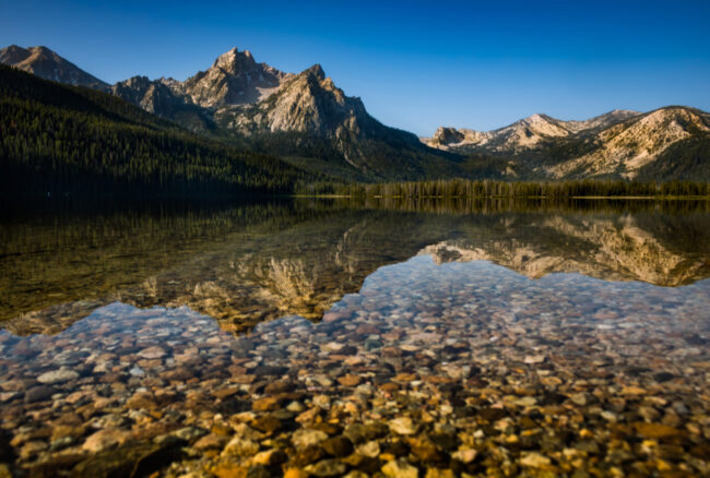 Clear alpine lake in Idaho reflecting rugged mountain peaks and forested slopes