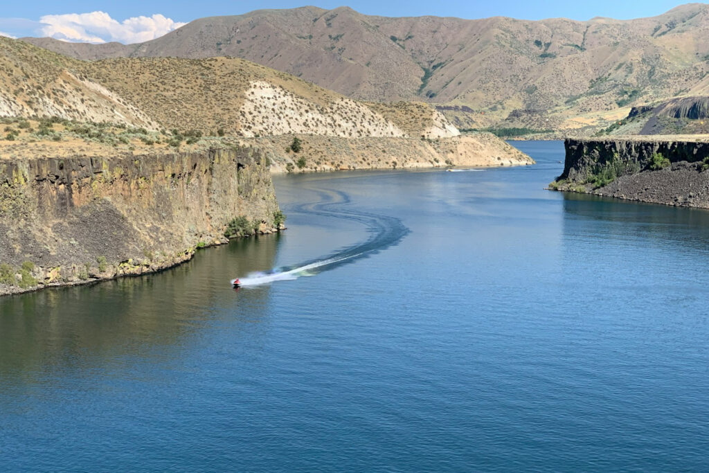 Reservoir in Idaho with rocky cliffs and a boat moving through the water