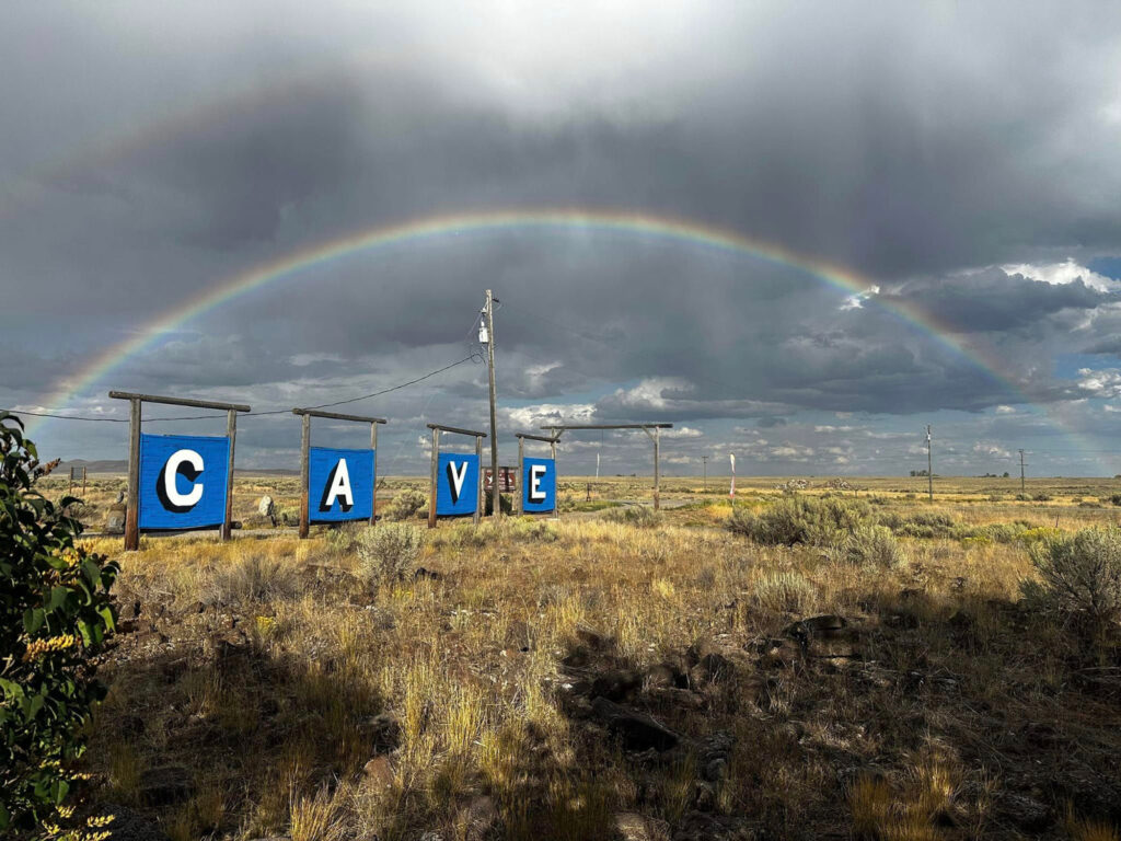 Entrance sign for Idaho’s Mammoth Cave near Shoshone Idaho with rainbow over the Snake River Plain desert landscape