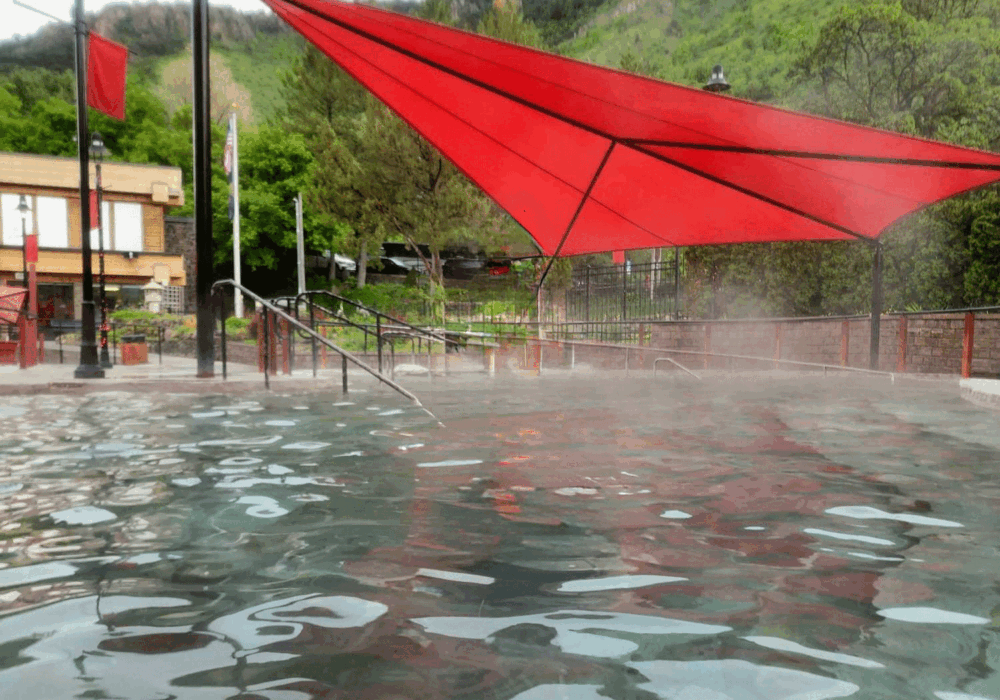 Outdoor soaking pool at Lava Hot Springs in southeastern Idaho with steam rising beneath a red shade canopy