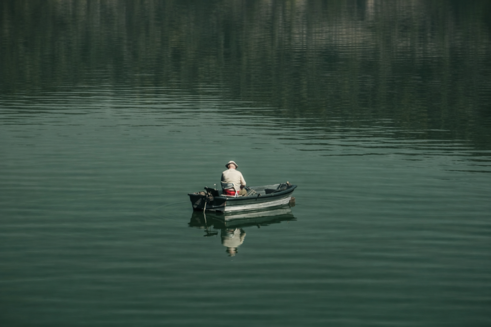 person fishing from small boat on calm reservoir with reflective water surface