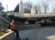 Person sitting along Boise River Greenbelt path in Idaho with pedestrian bridge and trees in background
