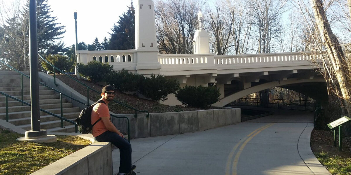 Person sitting along Boise River Greenbelt path in Idaho with pedestrian bridge and trees in background