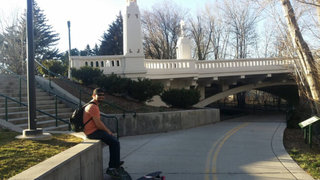 Person sitting along Boise River Greenbelt path in Idaho with pedestrian bridge and trees in background
