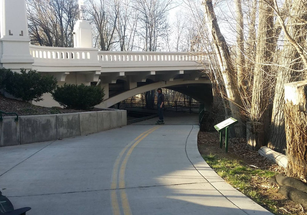 skateboarder riding along Boise River Greenbelt path under pedestrian bridge in Boise Idaho