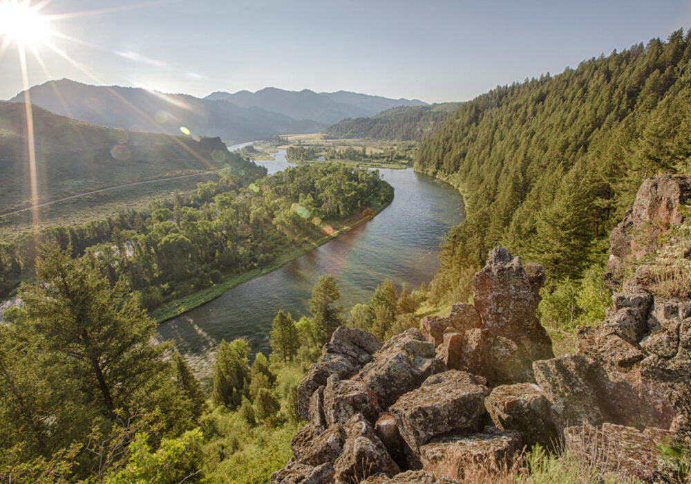 Sunlit view of the Snake River winding through forested mountains and valley landscape in Island Park, Idaho