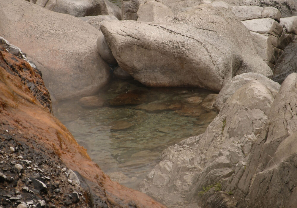 Natural rock pool at Kirkham Hot Springs in Idaho with clear water surrounded by large granite boulders and mineral-stained rock surfaces