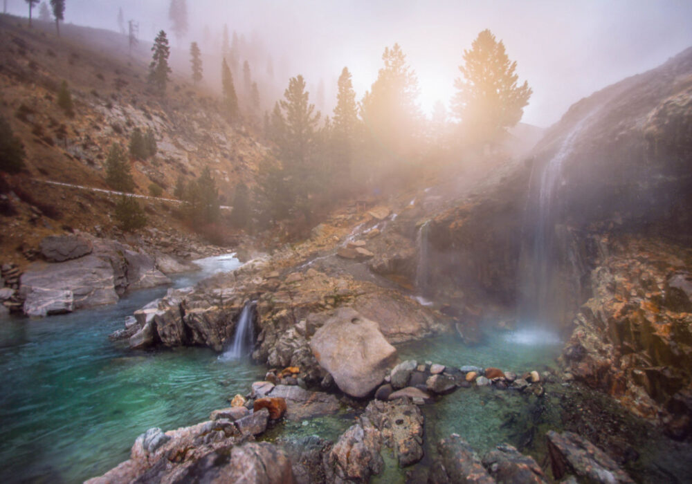 Steaming waterfalls flowing into turquoise pools at Kirkham Hot Springs surrounded by pine trees in Idaho
