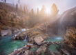 Steaming waterfalls flowing into turquoise pools at Kirkham Hot Springs surrounded by pine trees in Idaho