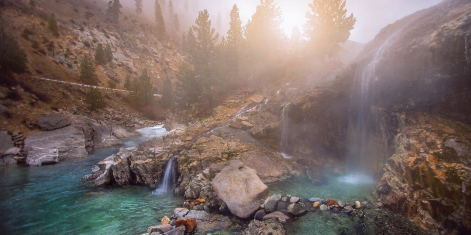 Steaming waterfalls flowing into turquoise pools at Kirkham Hot Springs surrounded by pine trees in Idaho