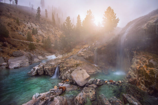 Steaming waterfalls flowing into turquoise pools at Kirkham Hot Springs surrounded by pine trees in Idaho
