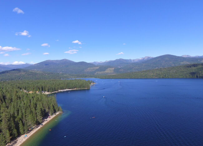 Aerial view of Priest Lake in Idaho with clear blue water, forested shoreline, and mountain scenery