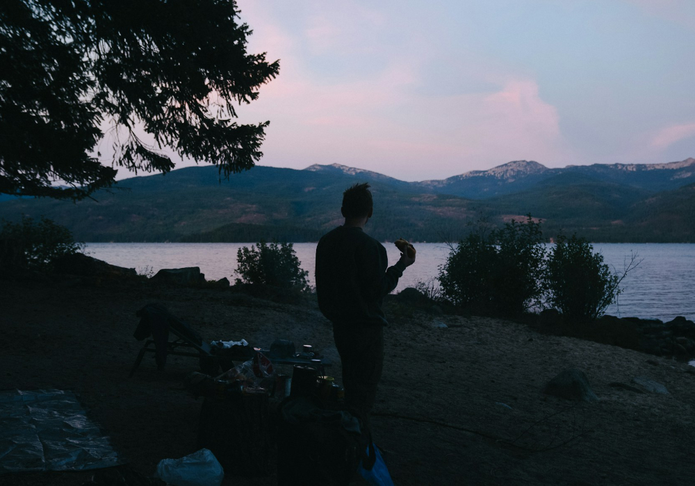 Person camping along the shore of Priest Lake in Idaho at sunset with mountain views across the water
