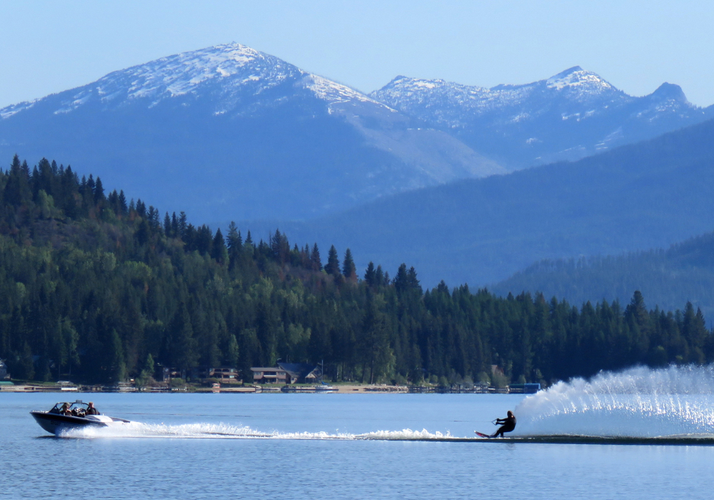 Waterskier on Priest Lake in Idaho with mountain views and a boat creating a spray across the water