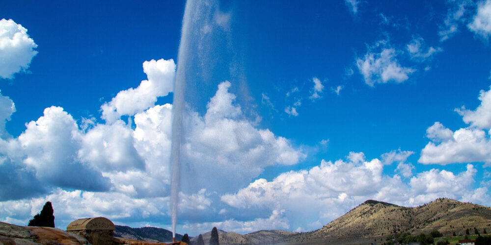 Soda Springs Geyser erupting in Idaho with wide scenic view of hills and mineral ground, one of the most unique things to do in Idaho