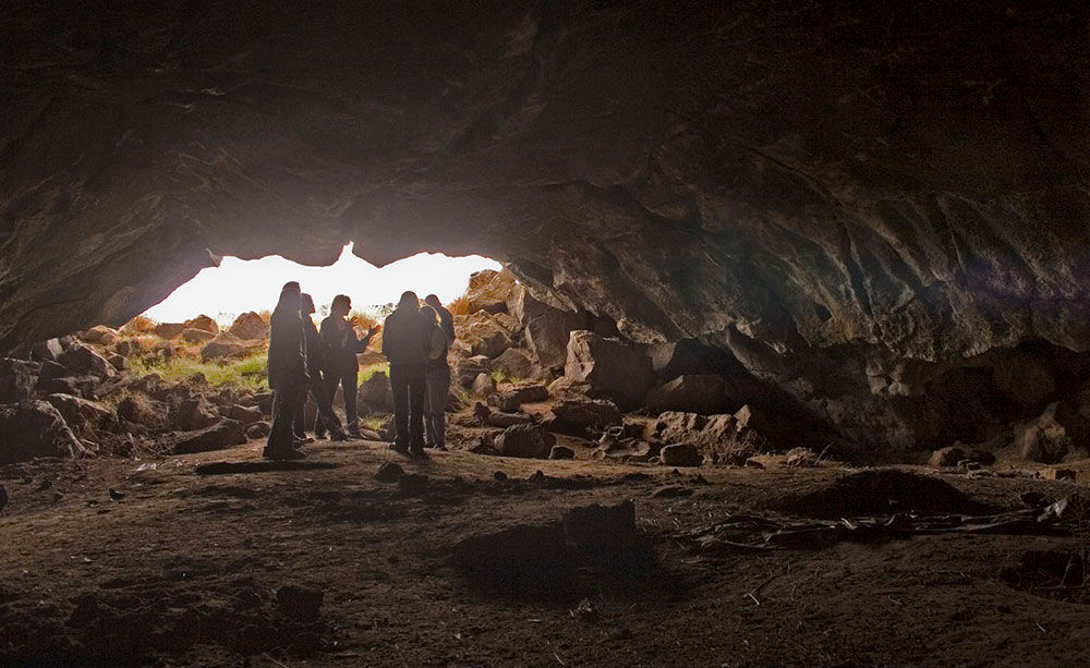 people standing inside Wilson Butte Cave in Idaho with light at cave entrance and rocky lava tube interior
