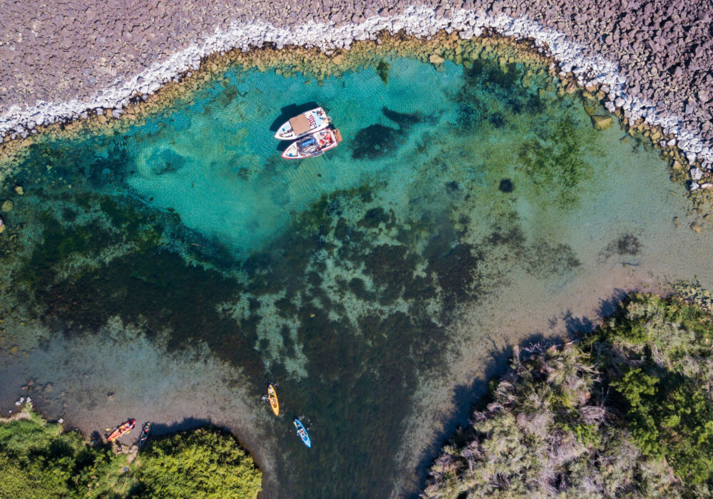 Aerial view of Blue Heart Springs in southern Idaho with clear turquoise water, kayaks, and small boats along the shoreline