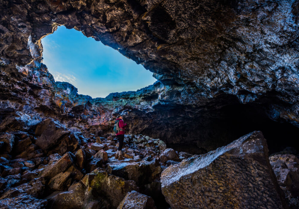 Hiker exploring the rocky interior of Indian Tunnel Cave at Craters of the Moon National Monument in Idaho beneath a natural lava tube opening