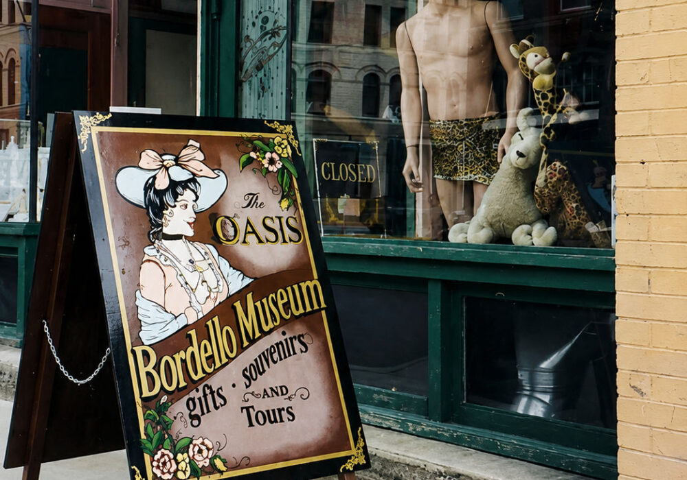 oasis-bordello-museum-wallace-idaho Entrance display and storefront window at the Oasis Bordello Museum in Wallace, Idaho featuring vintage signage and historic downtown reflections