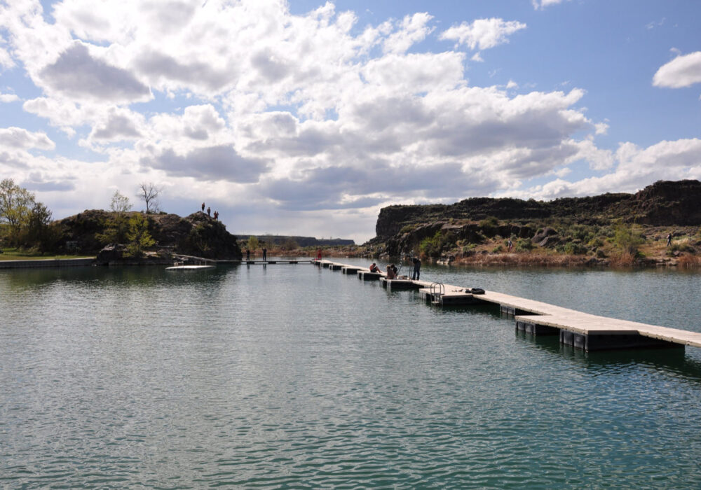 STEPHEN HANAFIN shanafin@gmail.com Floating dock extending across Dierkes Lake in Twin Falls, Idaho, with calm blue water, rocky canyon walls, and dramatic clouds overhead.